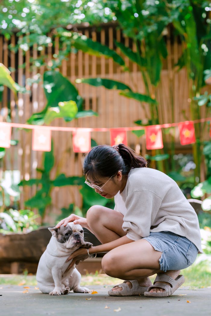 Woman kneeling to pet a bulldog in a lush garden setting.